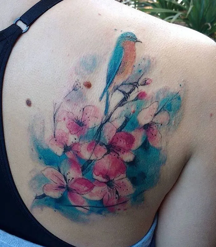 Colorful small bird tattoo with floral design on shoulder.
