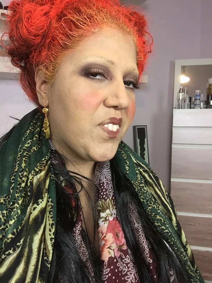 A woman dressed as Winifred Sanderson in a creative Halloween costume with bright red hair.