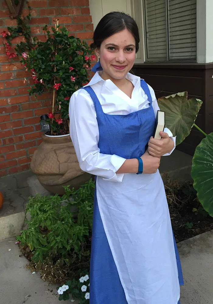 Woman dressed in a blue dress and white apron holding a book, showcasing a creative Halloween costume idea.