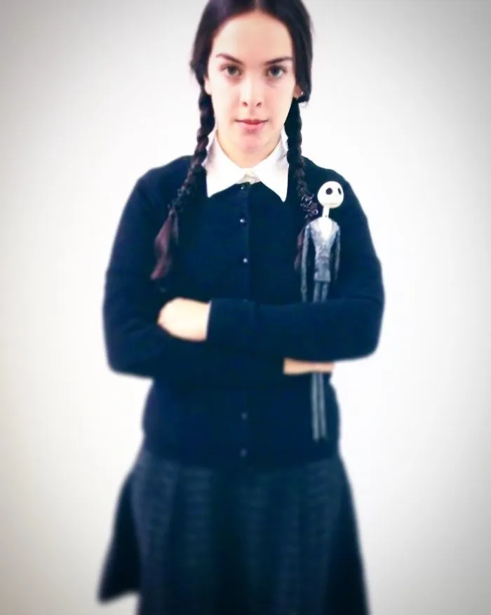 A girl dressed in a Wednesday Addams creative Halloween costume holding a Jack Skellington figure