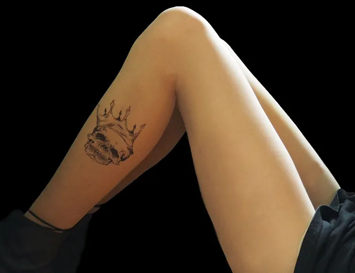 Tattoo tights creating an inked illusion with a skull and crown design on the thigh against a black background.