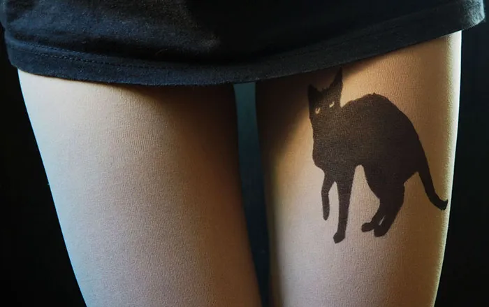 Tattoo tights with black cat design creating inked illusion on legs under a black skirt.