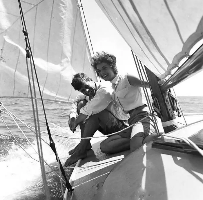 Couple smiling on a sailboat, enjoying a sunny day on the ocean, representing iconic historical photography moments.