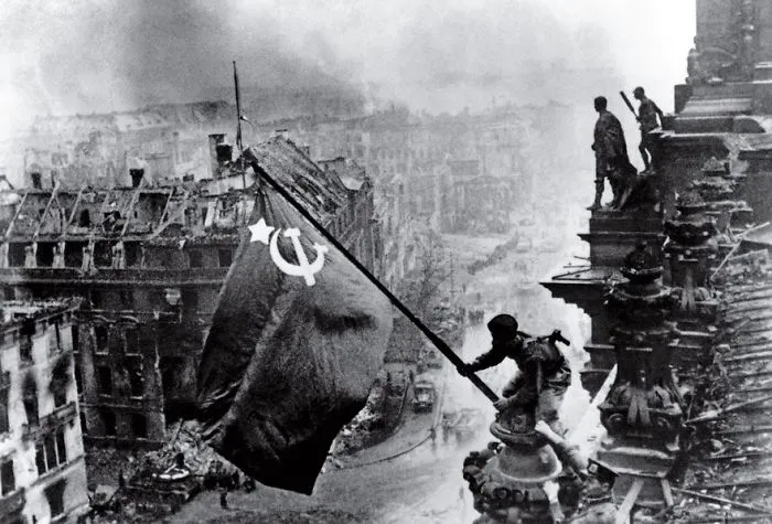 Soldier raising Soviet flag over Berlin during WWII, capturing a historic moment in photography.