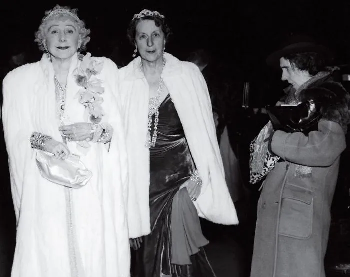 Two elegantly dressed women in white coats at an event, representing one of the most famous photos in history.