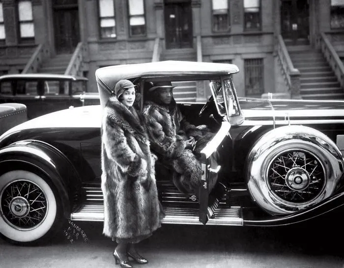 Vintage photo featuring a couple in luxurious fur coats with a classic car, highlighting famous historical photography.