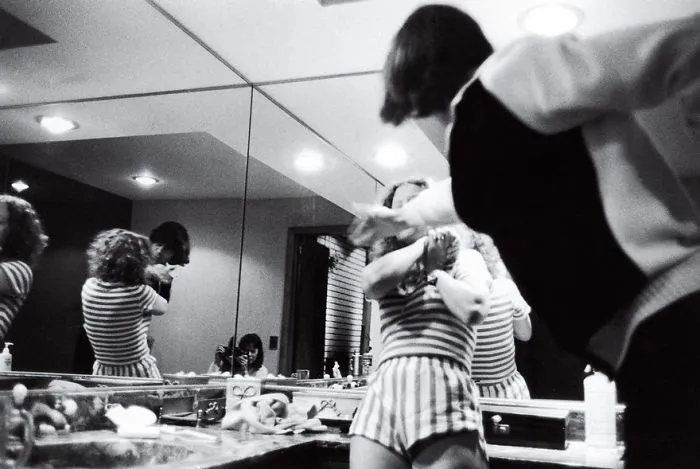 Black and white image of a dramatic scene in a mirrored bathroom, capturing a moment of tension.