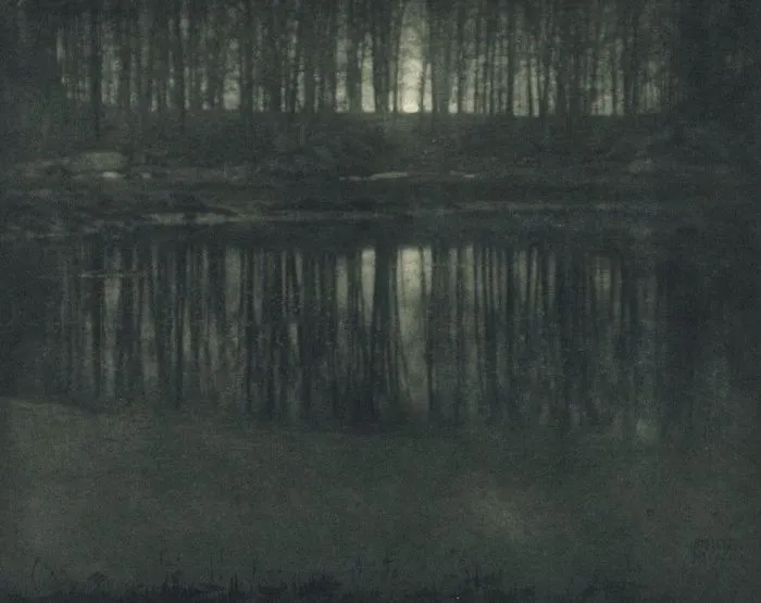 Famous historical photo of a serene lake reflecting a moonlit forest at night.