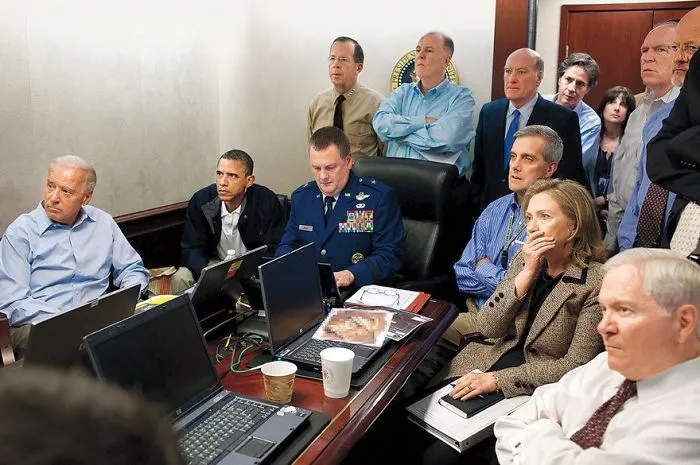 Famous historical photo of a group intently watching a monitor in a conference room, including military and civilian officials.