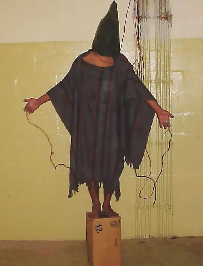 A cloaked figure stands on a box with outstretched arms, embodying one of the most famous historical photos.