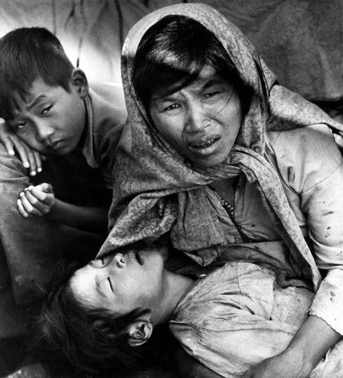 A historical photo featuring an emotional mother with two children during a wartime event, conveying deep sadness and resilience.