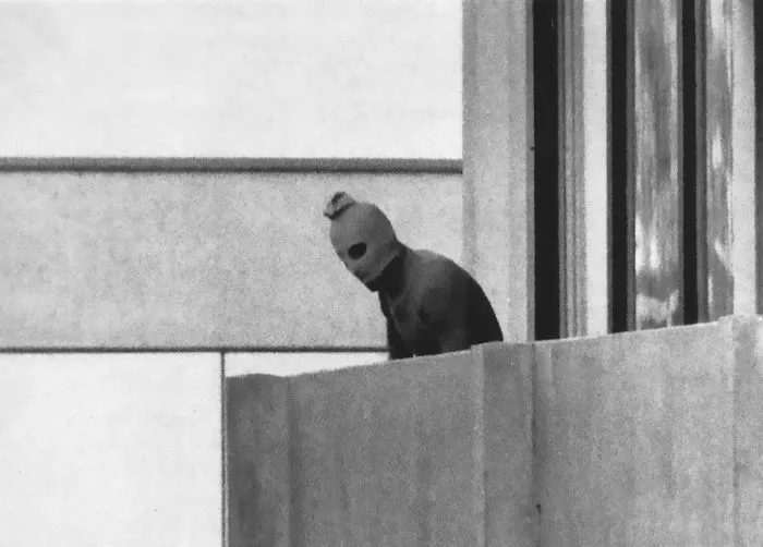 Balaclava-clad figure on a concrete balcony, historical photo.
