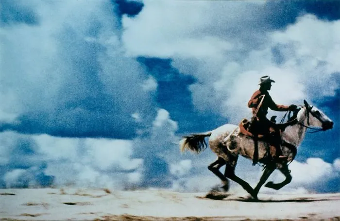 Cowboy riding a horse across a desert landscape under a dramatic sky, from famous photos in history.