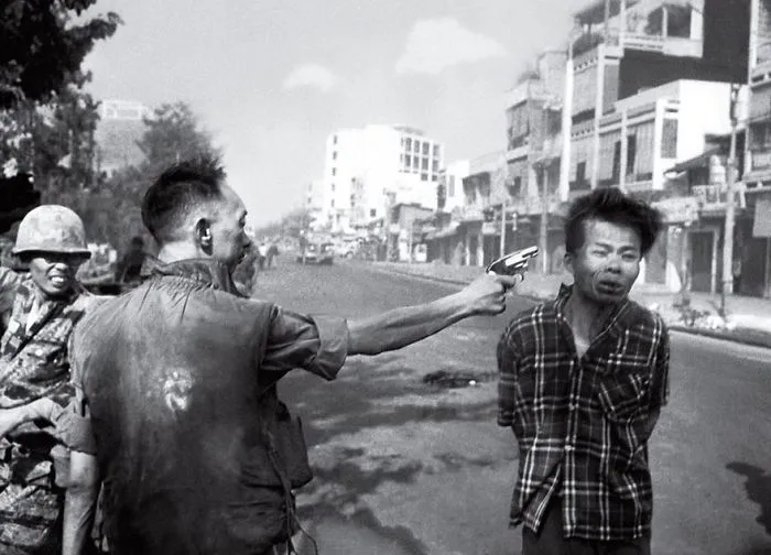 A soldier aiming a gun at a man's head on a city street; iconic historical photo capturing a tense moment.