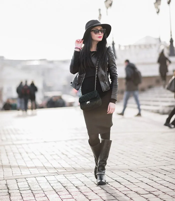 Stylish woman in a black outfit and hat poses confidently in an urban setting, showcasing beauty before Photoshop edits.