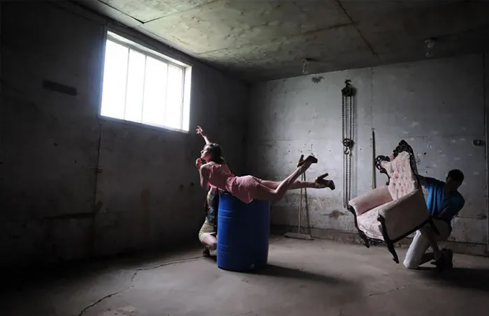 Behind the scenes of a Photoshop shoot with a model posing on a barrel in a dimly lit room.