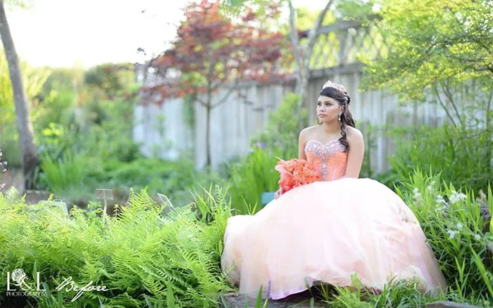 Woman in a peach gown sitting in a garden, showcasing natural beauty before Photoshop editing.