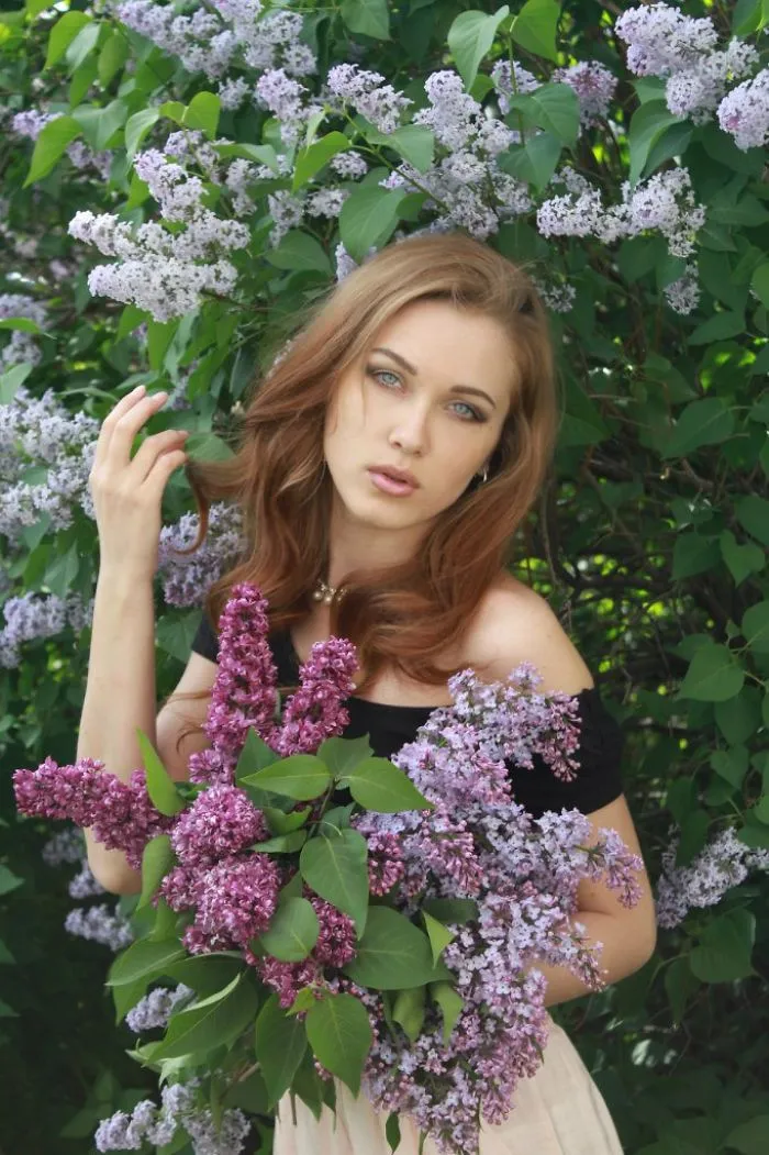 Woman holding lilac flowers with lush greenery, illustrating beauty before Photoshop editing.
