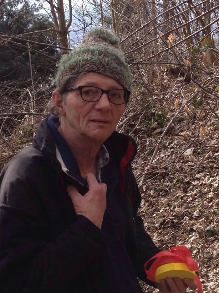 Man wearing glasses and a knit hat outdoors holding red and yellow objects, illustrating before and after quitting drinking effects
