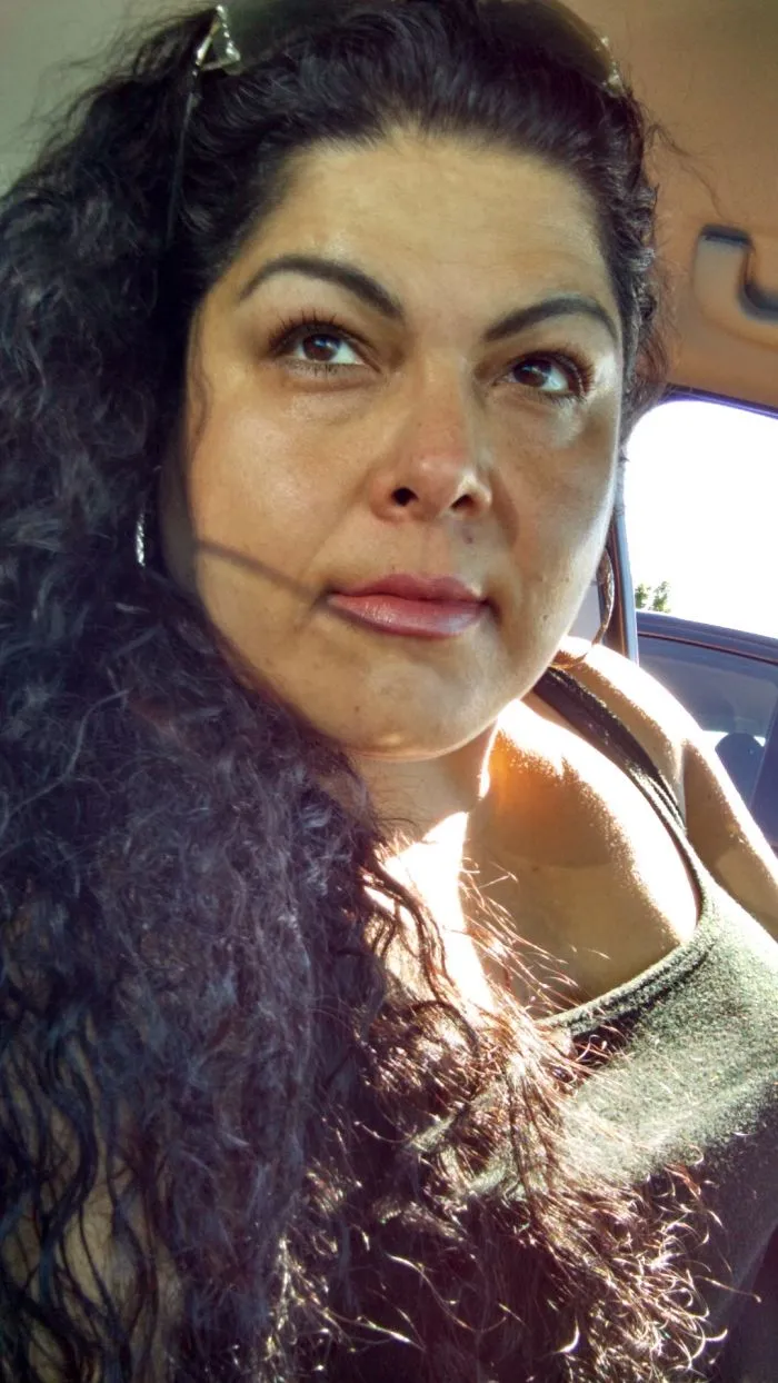 Woman with curly hair sitting in a car, showing clear skin and healthy appearance after stopping drinking.