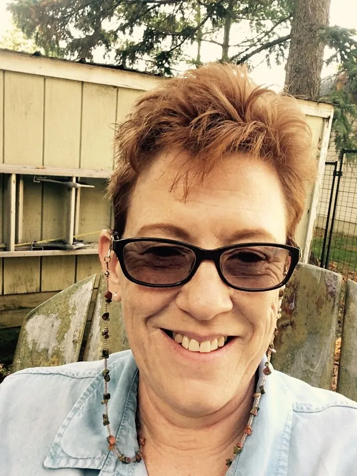 Smiling middle-aged woman wearing glasses sitting outdoors, showing positive effects of stopping drinking in transformation.