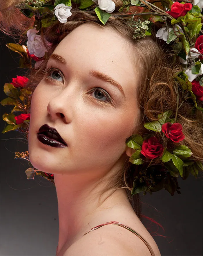Young woman with dark lipstick and floral hair arrangement, showcasing before and after Photoshop beauty transformation.