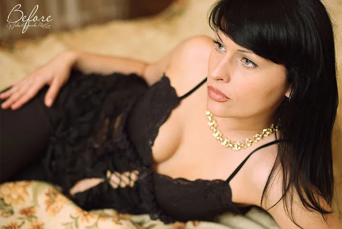 Woman in black lace dress lying on a bed, showcasing natural beauty before Photoshop.