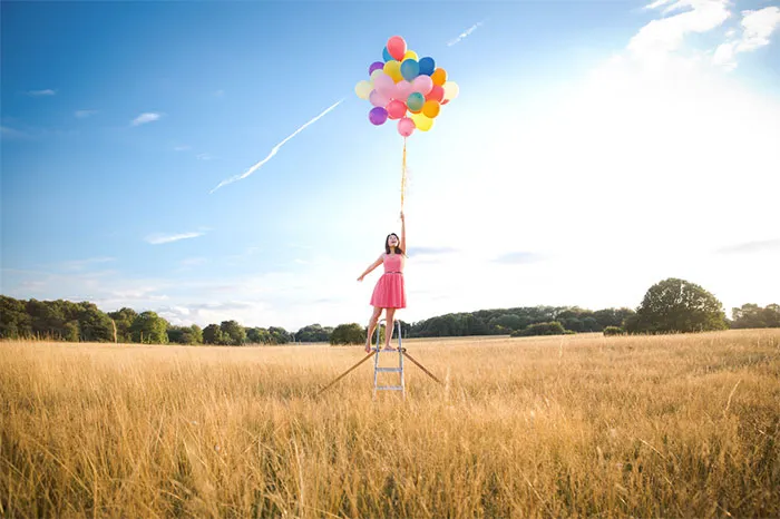 Girl holding colorful balloons on a ladder in a field, illustrating Photoshop's truth behind beautiful photos.