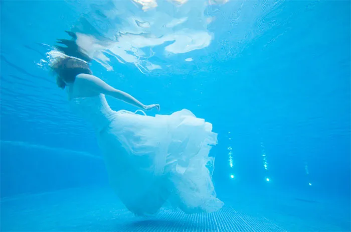 Woman in a flowing dress underwater, showcasing the truth behind beautiful photos before Photoshop.