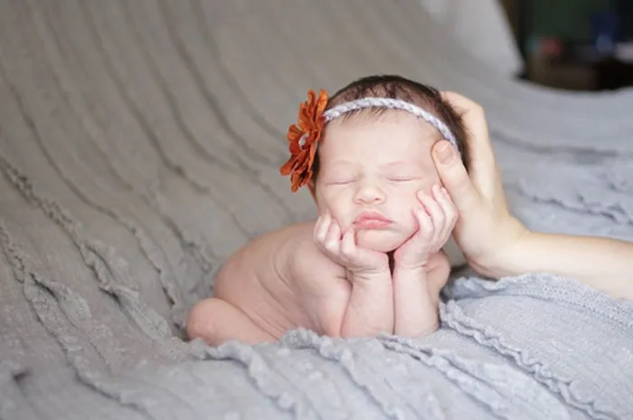 Baby posed on a gray blanket, supported by a hand for a Photoshop before-and-after reveal.