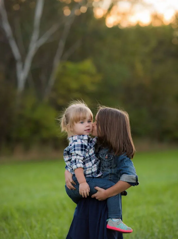"Two children hugging in a grassy field, capturing a candid moment of beauty before Photoshop."