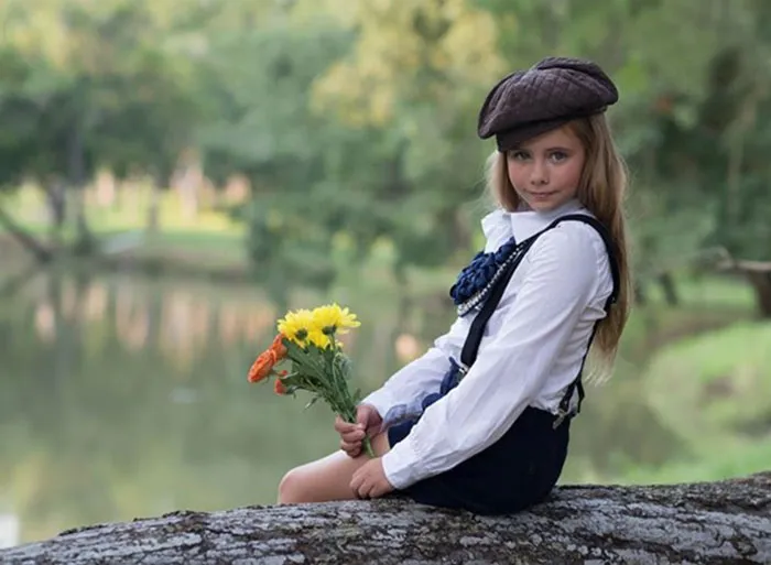 A girl in a white shirt and cap holding flowers, showcasing the transformation of beautiful photos before and after Photoshop.