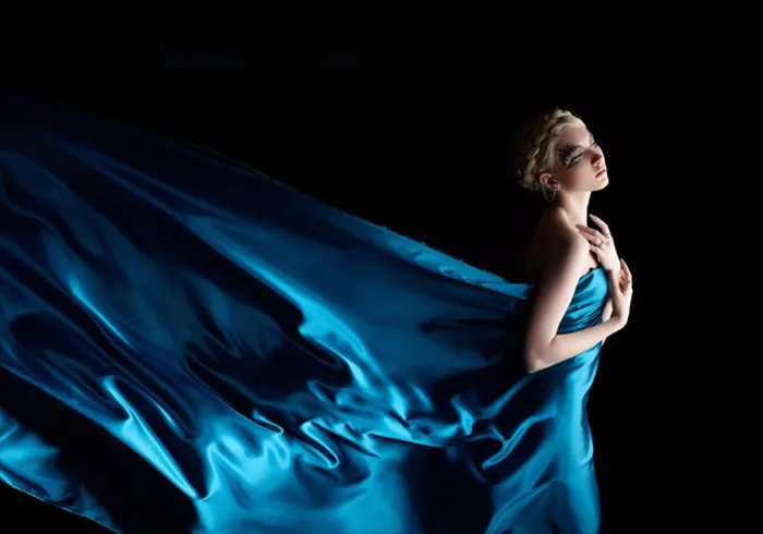 Woman in a flowing blue dress posed against a dark background, showcasing the truth behind beautiful photos.