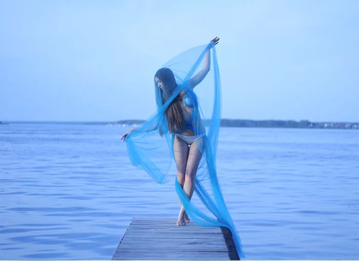 Woman in blue veil standing on dock by the water, showcasing the truth behind beautiful photos pre-Photoshop.