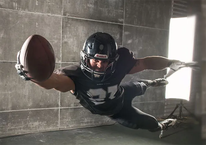 Football player in black uniform and helmet diving mid-air, holding a football, showcasing before and after Photoshop effects.