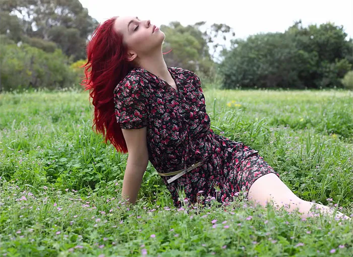 Woman with red hair in a floral dress reclines in a field, showcasing the truth behind beautiful photos.