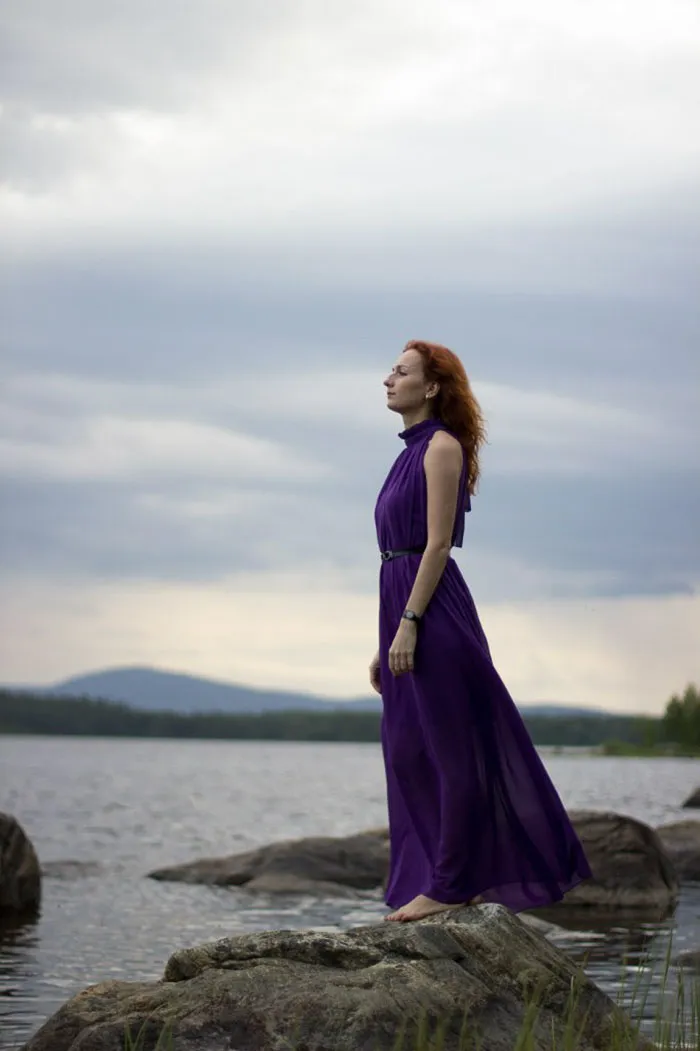 Woman in a purple dress standing on rocks by a lake, showcasing the truth behind beautiful photos before Photoshop.