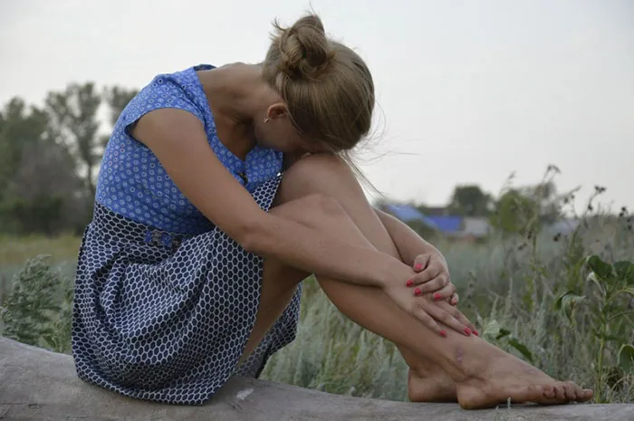 Woman in a blue dress sitting outdoors, showcasing natural beauty before Photoshop.