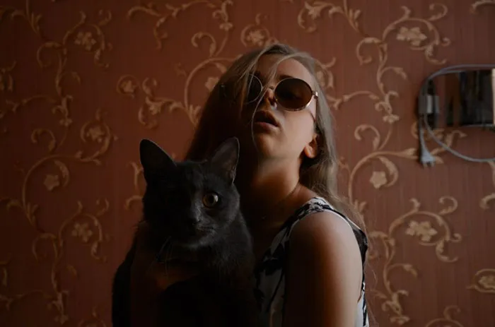 Person wearing sunglasses holding a cat, illustrating truth behind beautiful photos before and after Photoshop.