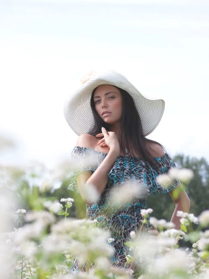 Woman in floral dress and sun hat posing in a field, showcasing the truth behind beautiful photos before Photoshop.