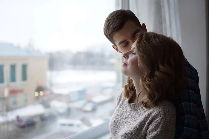 A couple embracing by a window, showcasing natural beauty before Photoshop enhancements.