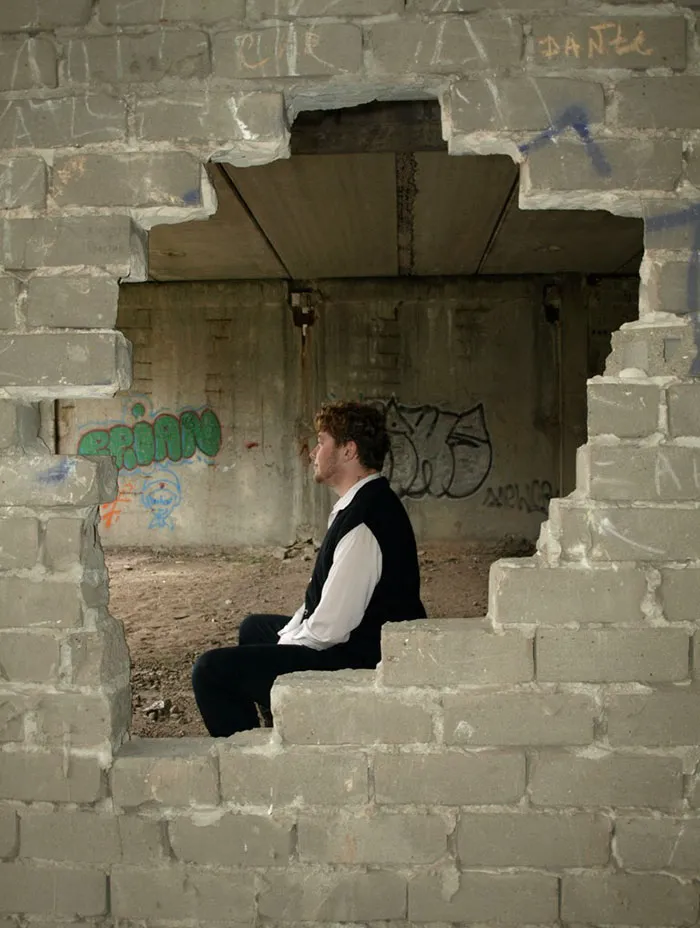 Man sitting on the ground behind a cracked brick wall with graffiti, highlighting the truth behind beautiful photos.