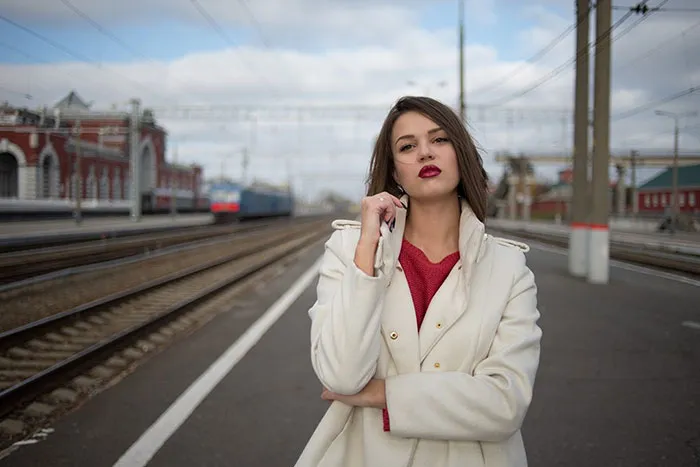 Woman in a white coat standing confidently on a train platform, illustrating photography's potential before Photoshop.