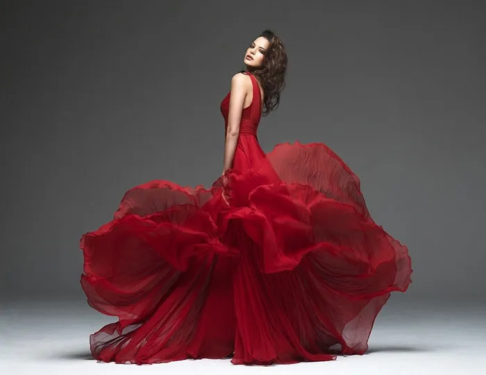 Elegant woman in a flowing red dress posing in a studio, showcasing beauty before Photoshop edits.