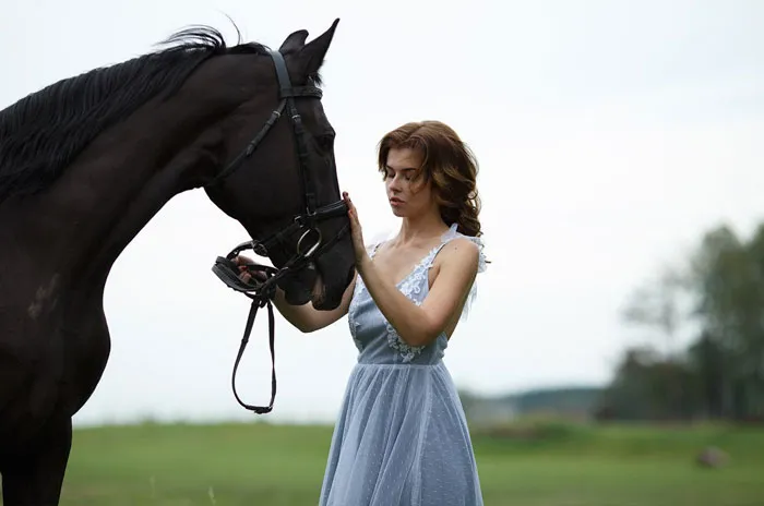 Woman in a blue dress gently holding a horse's bridle, illustrating natural beauty.