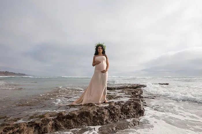 Woman in a long dress standing on rocks by the ocean, showcasing the contrast in beautiful photos before and after Photoshop.