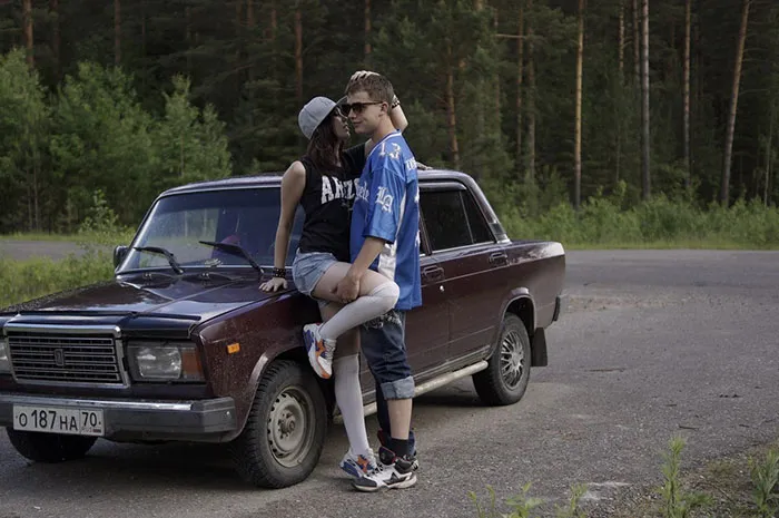 Couple posing on a vintage car in a forest setting, showcasing the truth behind beautiful photos before Photoshop.