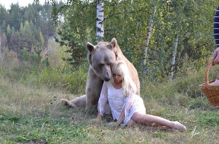 Woman in a white dress sitting with a bear in a forest setting, showcasing the truth behind beautiful photos.