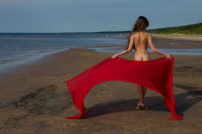 Woman on a beach holding a flowing red fabric, showcasing a natural scene before photo editing.
