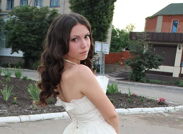 Woman in a white dress posing outdoors before Photoshop.